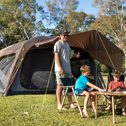Family of four standing near a large camping tent in a park setting.