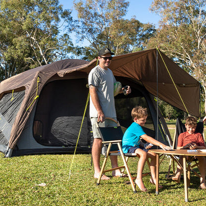 Family of four standing near a large camping tent in a park setting.