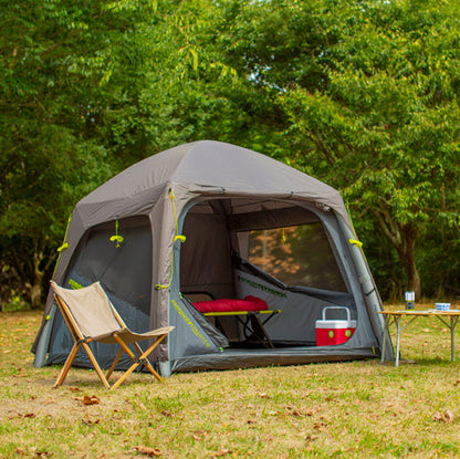 Person sitting near a camping tent in a forested area